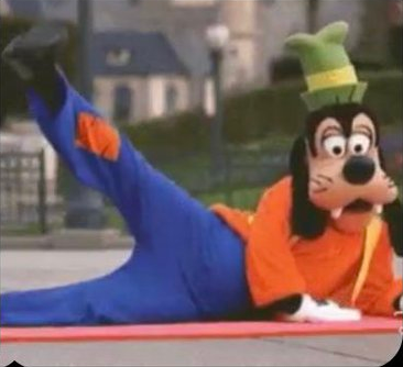 A person in a Goofy costume lying on their side on a yoga mat and lifting their leg
