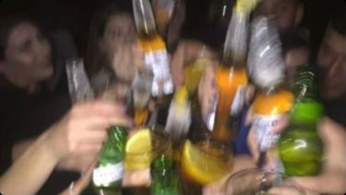 A blurry picture in which a group of people clink their beer bottles and drinks glasses together
