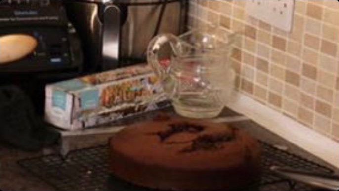 An undecorated brown cake on a countertop. There’s some chunks taken out of it, or maybe squished.